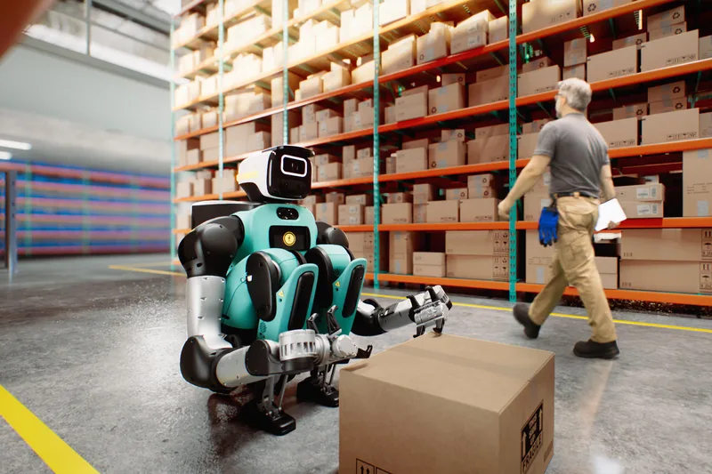 Гуманоидный робот Agility Robotics Digit 5 с коробкой на складе, рядом проходит человек